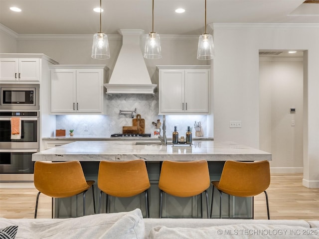 kitchen with custom range hood, appliances with stainless steel finishes, light wood finished floors, white cabinets, and tasteful backsplash