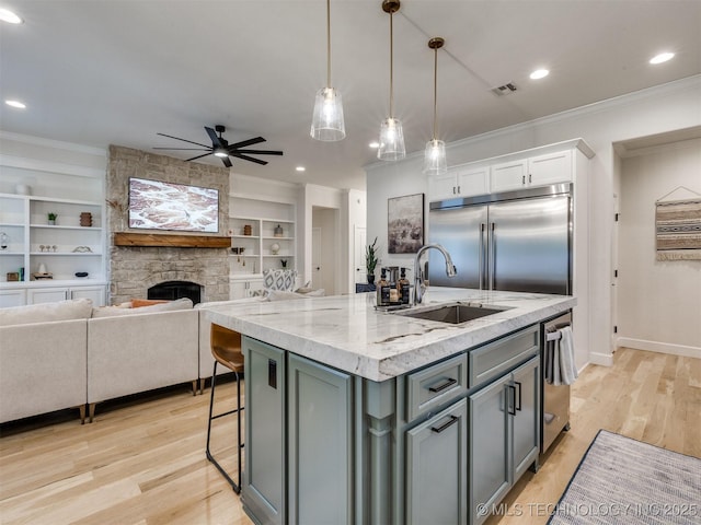 kitchen featuring appliances with stainless steel finishes, a sink, ornamental molding, a stone fireplace, and ceiling fan