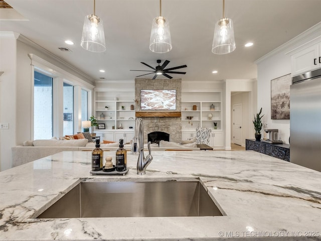 kitchen with a sink, open floor plan, ornamental molding, stainless steel built in refrigerator, and light stone counters