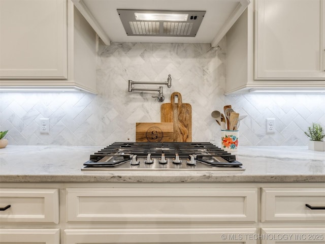 kitchen with stainless steel gas cooktop, tasteful backsplash, light stone countertops, and white cabinetry