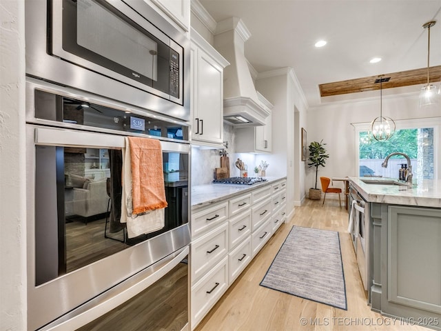 kitchen with appliances with stainless steel finishes, a sink, custom exhaust hood, light wood-style floors, and white cabinetry