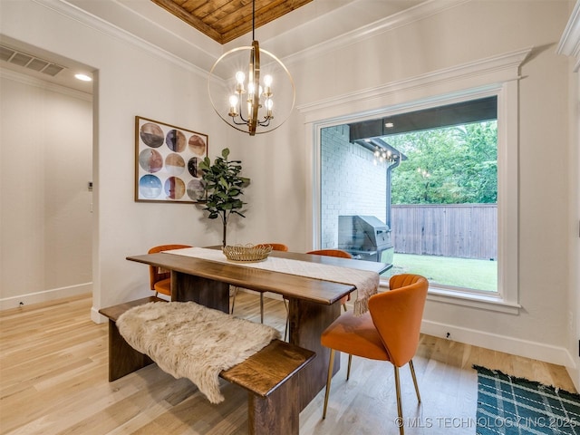 dining room featuring a chandelier, light wood finished floors, crown molding, baseboards, and a raised ceiling