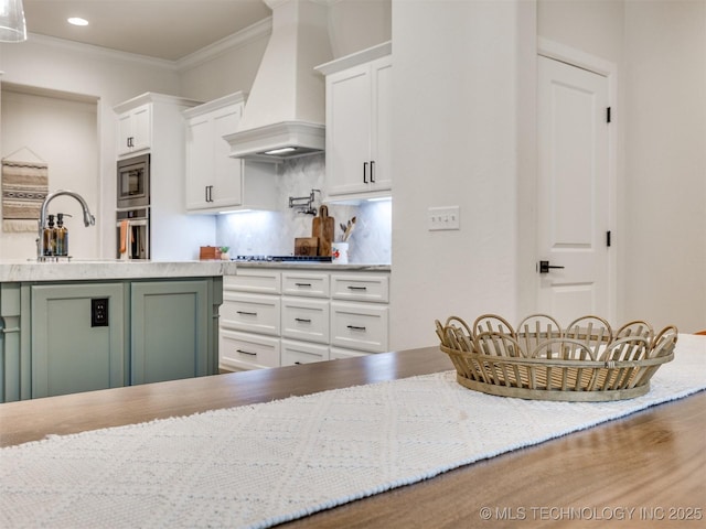 kitchen featuring custom range hood, decorative backsplash, ornamental molding, white cabinetry, and a sink