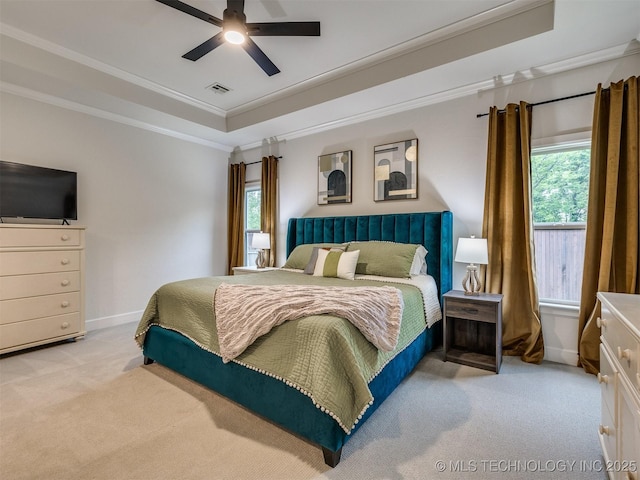 carpeted bedroom with a raised ceiling, multiple windows, crown molding, baseboards, and ceiling fan