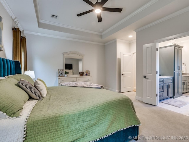 bedroom featuring a tray ceiling, light carpet, ornamental molding, ensuite bath, and baseboards