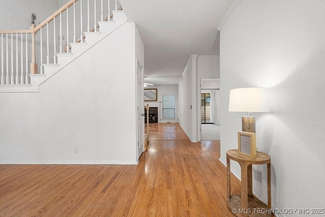 entrance foyer with wood finished floors, baseboards, crown molding, stairway, and a fireplace