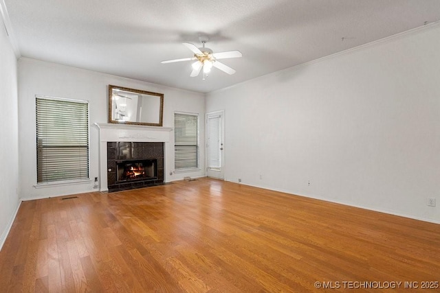unfurnished living room featuring wood finished floors, a tile fireplace, a ceiling fan, baseboards, and crown molding