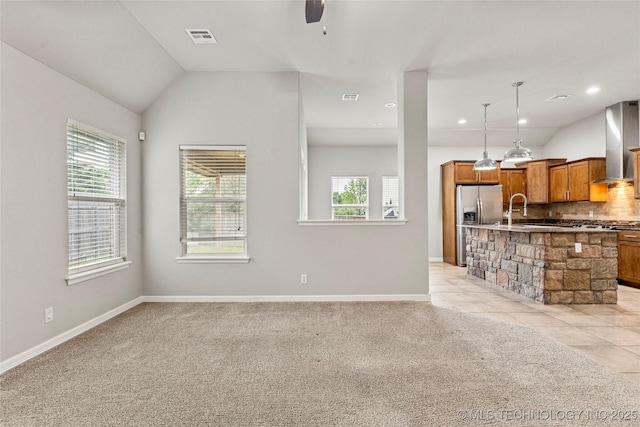 unfurnished living room with plenty of natural light, vaulted ceiling, ceiling fan, baseboards, and light colored carpet