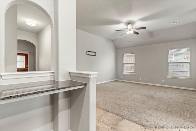 empty room featuring arched walkways, ceiling fan, light carpet, baseboards, and lofted ceiling