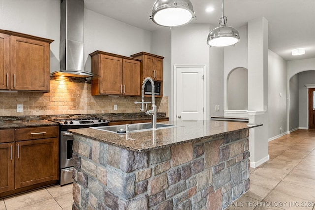 kitchen featuring gas stove, wall chimney exhaust hood, a sink, arched walkways, and dark stone countertops