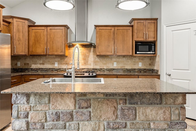 kitchen with wall chimney range hood, brown cabinets, stainless steel refrigerator, dark stone counters, and built in microwave
