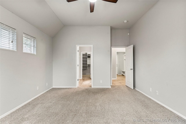 unfurnished bedroom featuring a spacious closet, light colored carpet, baseboards, lofted ceiling, and a ceiling fan