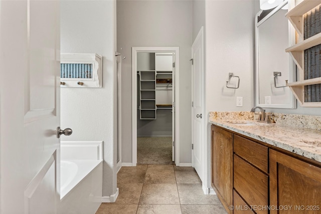 full bath with baseboards, vanity, a spacious closet, a garden tub, and tile patterned flooring