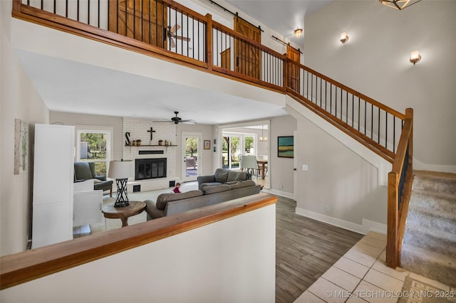 living area with plenty of natural light, a fireplace, baseboards, a ceiling fan, and a towering ceiling