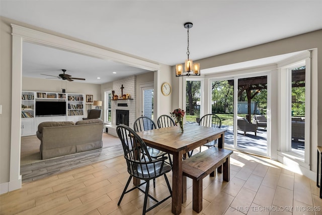 dining space featuring a chandelier, a brick fireplace, a ceiling fan, and light wood finished floors