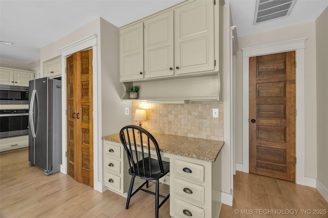 kitchen featuring appliances with stainless steel finishes, light wood-type flooring, tasteful backsplash, and light stone counters