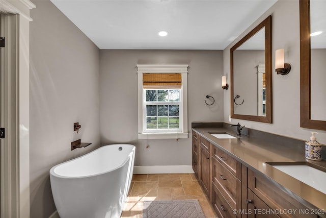 full bath featuring baseboards, a freestanding bath, double vanity, recessed lighting, and stone tile flooring
