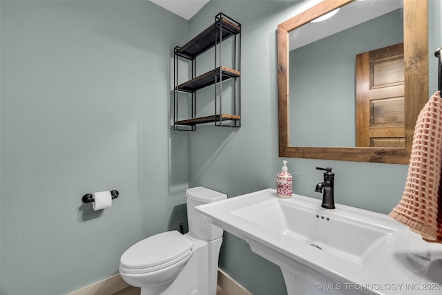 half bathroom with a sink, toilet, and baseboards