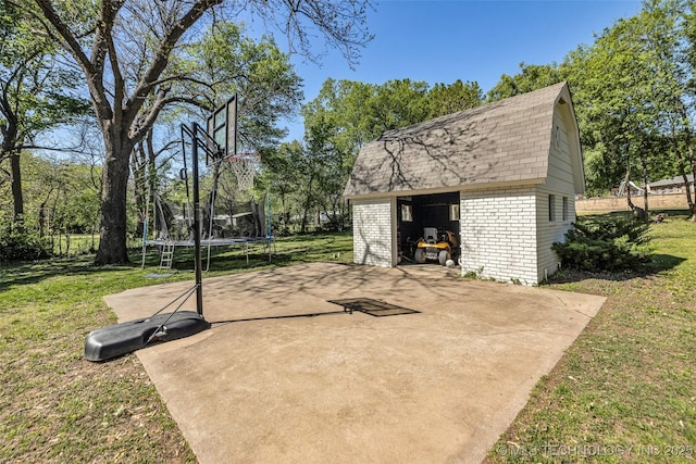 view of basketball court with a storage shed, a trampoline, and a lawn