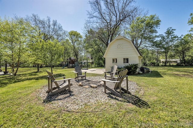 view of grassy yard featuring a barn, a playground, an outdoor structure, and view of wooded area