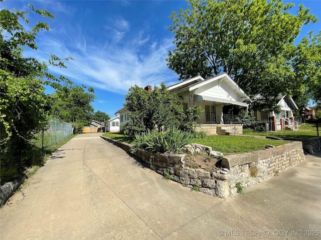 view of side of home featuring covered porch, fence, and concrete driveway