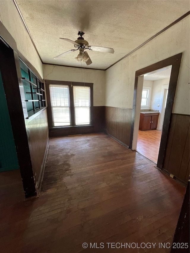 unfurnished room featuring a textured ceiling, wood finished floors, wainscoting, ceiling fan, and wooden walls