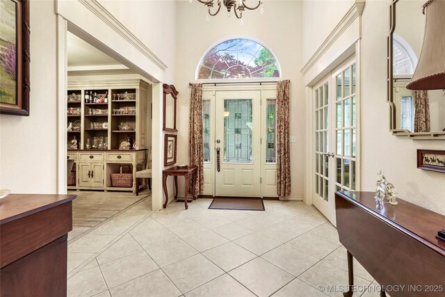 foyer entrance featuring light tile patterned flooring, a chandelier, a high ceiling, and french doors