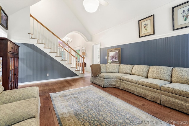 living area with stairway, wood finished floors, wainscoting, arched walkways, and high vaulted ceiling