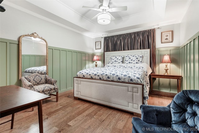 bedroom featuring a tray ceiling, wainscoting, wood finished floors, a decorative wall, and ornamental molding