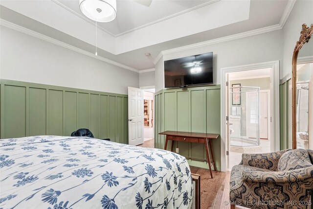 bedroom featuring wood finished floors, crown molding, ensuite bath, and wainscoting