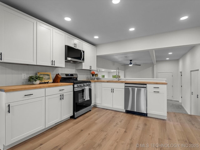 kitchen featuring stainless steel appliances, wood counters, a peninsula, ceiling fan, and light wood-style floors