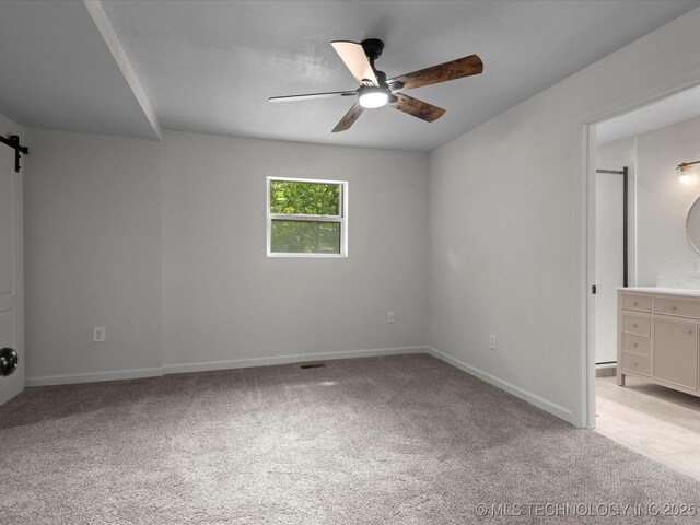 unfurnished bedroom with a barn door, light colored carpet, baseboards, and ensuite bathroom