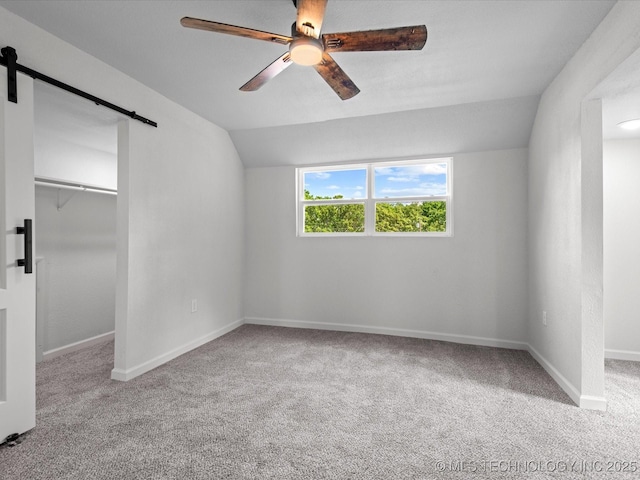 unfurnished bedroom with a barn door, carpet flooring, vaulted ceiling, a spacious closet, and baseboards