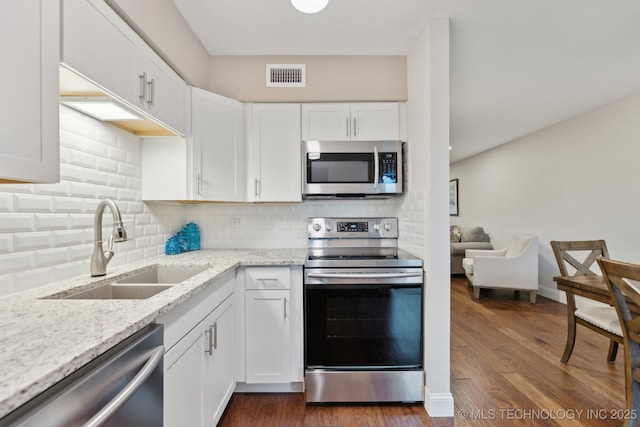kitchen featuring stainless steel appliances, a sink, white cabinets, light stone counters, and backsplash