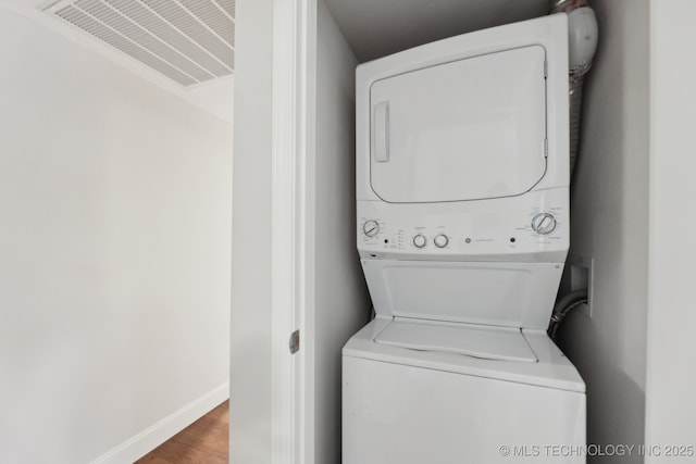 clothes washing area with estacked washer and dryer, baseboards, and wood finished floors