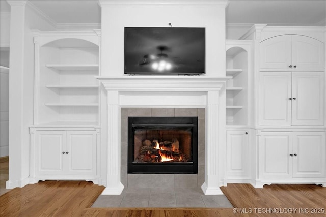 detailed view of wood finished floors, crown molding, built in features, and a tile fireplace