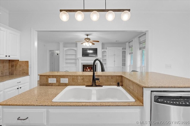 kitchen with stainless steel dishwasher, a sink, a ceiling fan, and light stone countertops