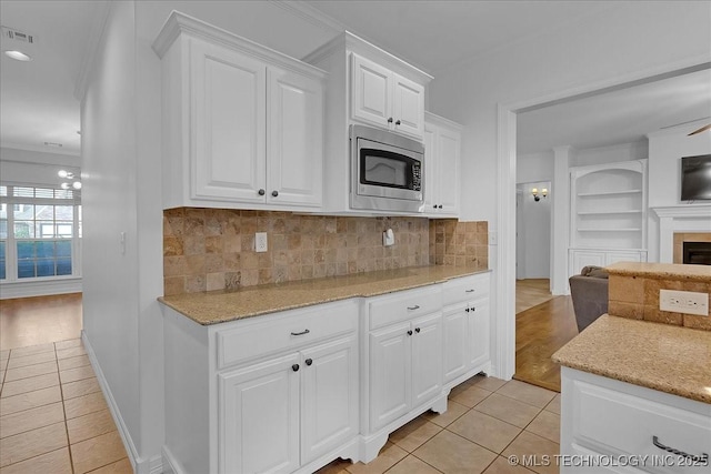 kitchen featuring stainless steel microwave, light tile patterned floors, ornamental molding, white cabinets, and light stone counters