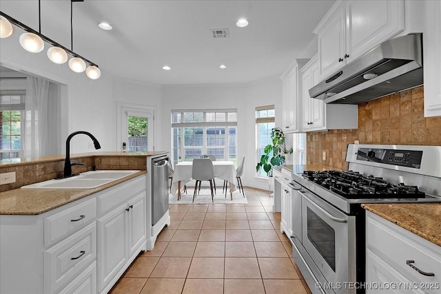 kitchen featuring appliances with stainless steel finishes, under cabinet range hood, a sink, decorative backsplash, and light tile patterned floors