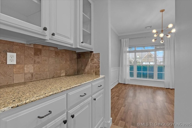 kitchen featuring ornamental molding, glass insert cabinets, white cabinets, backsplash, and light stone counters