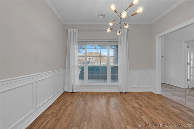 unfurnished dining area featuring a chandelier, ornamental molding, a decorative wall, a wainscoted wall, and wood finished floors