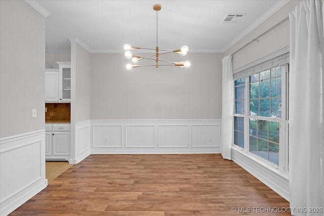unfurnished dining area featuring a chandelier, ornamental molding, light wood finished floors, and wainscoting