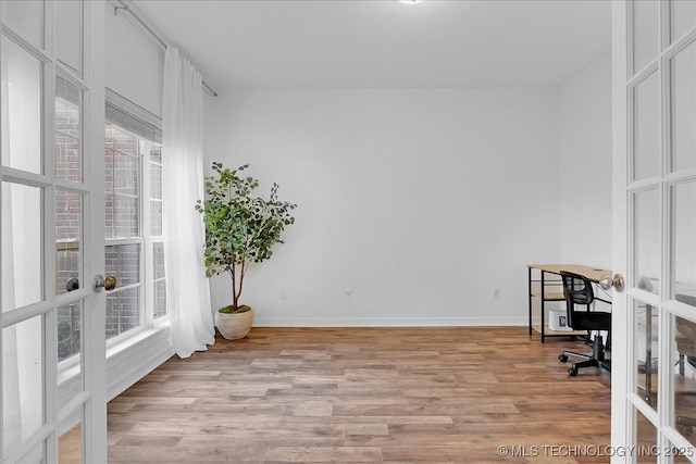 unfurnished office featuring french doors, light wood-style flooring, and baseboards