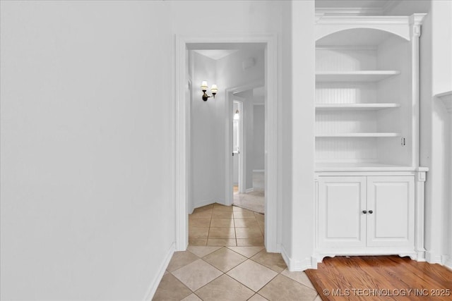 hallway with light tile patterned floors, baseboards, and built in shelves