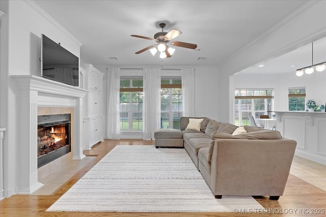 living area with ceiling fan, healthy amount of natural light, a fireplace, crown molding, and light wood finished floors
