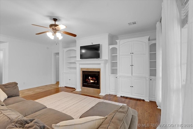 living room featuring a ceiling fan, wood finished floors, a fireplace, ornamental molding, and built in features