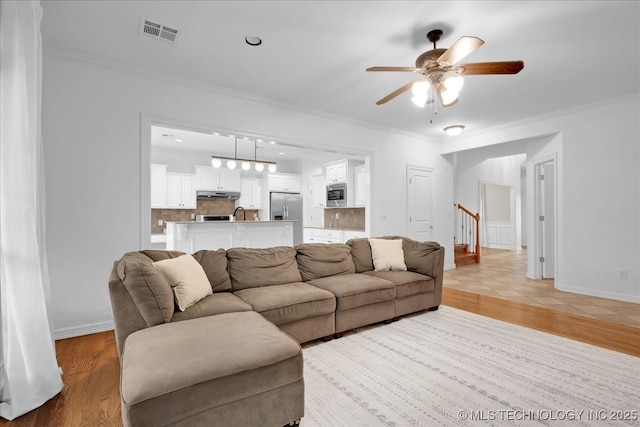 living area featuring ornamental molding, a ceiling fan, light wood finished floors, stairs, and baseboards