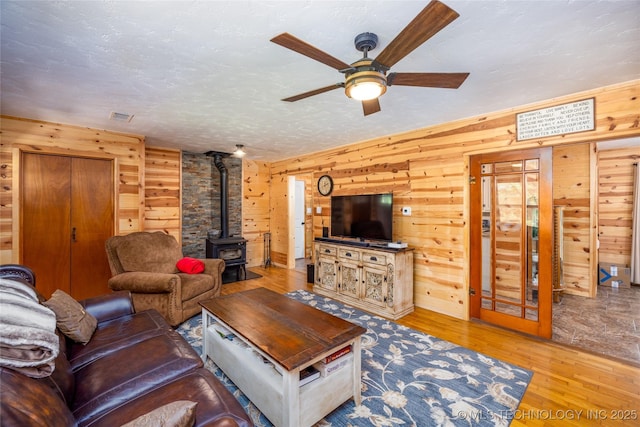 5700 S Wiley Rd, Milburn, OK 73450 - living room featuring wooden walls, a wood stove, a ceiling fan, wood finished floors, and a textured ceiling