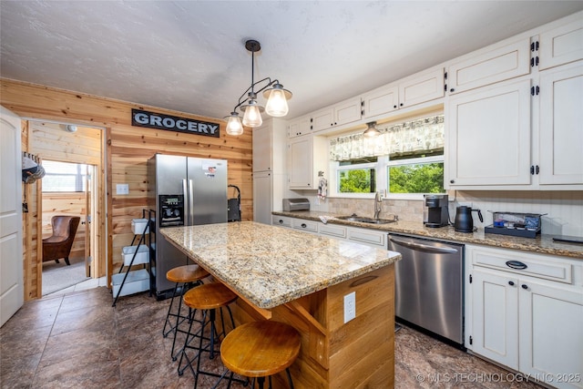 5700 S Wiley Rd, Milburn, OK 73450 - kitchen featuring appliances with stainless steel finishes, a sink, a center island, white cabinetry, and wooden walls