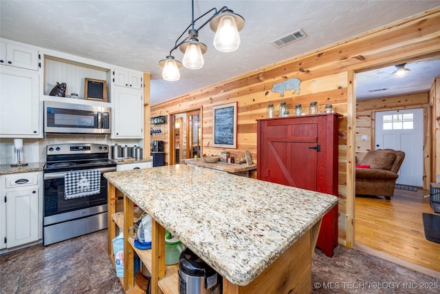 5700 S Wiley Rd, Milburn, OK 73450 - kitchen with appliances with stainless steel finishes, open shelves, white cabinets, a kitchen island, and wood walls